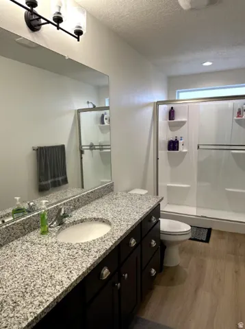 Full bath featuring vanity, a textured ceiling, light wood finished floors, and a shower stall