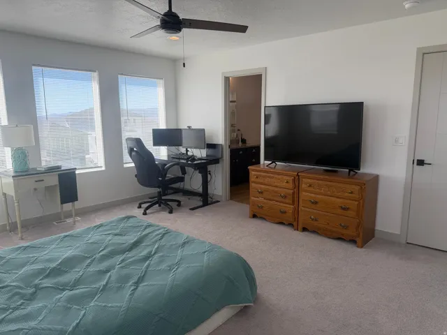 Bedroom with a desk, light colored carpet, a ceiling fan, connected bathroom, and a textured ceiling