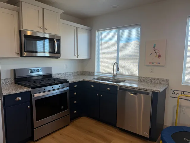 Dual tone kitchen featuring stainless steel appliances, dual tone cabinets, light stone countertops, and light wood-type flooring