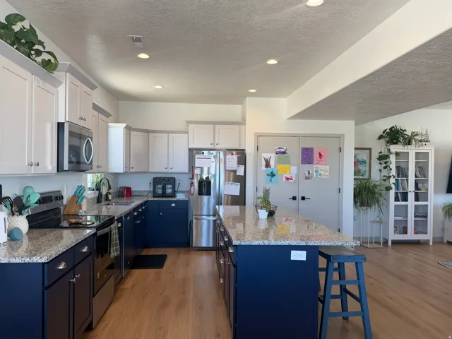 Dual tone kitchen featuring dual tone cabinetry, stainless steel appliances, light wood-type flooring, light stone counters, and a center island