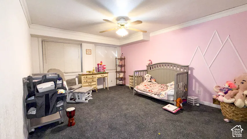 Bedroom with a crib, dark colored carpet, ceiling fan, and ornamental molding