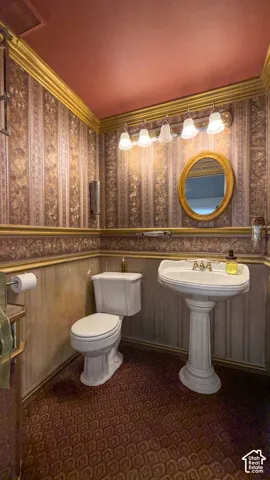 Bathroom with wallpapered walls, dark colored carpet, and crown molding
