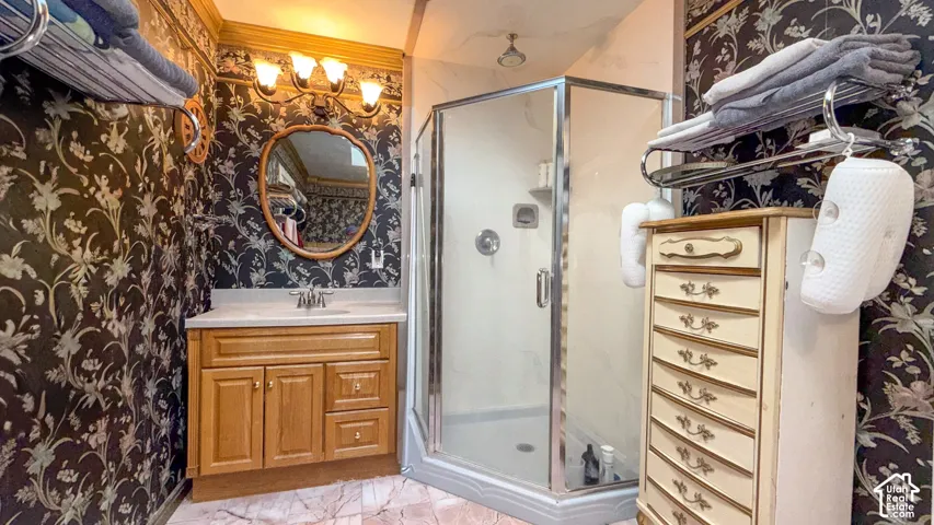 Bathroom with wallpapered walls, vanity, a stall shower, ornamental molding, and light marble finish floors