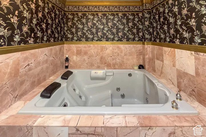 Bathroom featuring wallpapered walls and a tub with jets