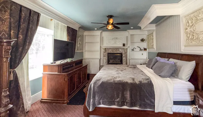 Bedroom with crown molding, a glass covered fireplace, dark carpet, and a ceiling fan