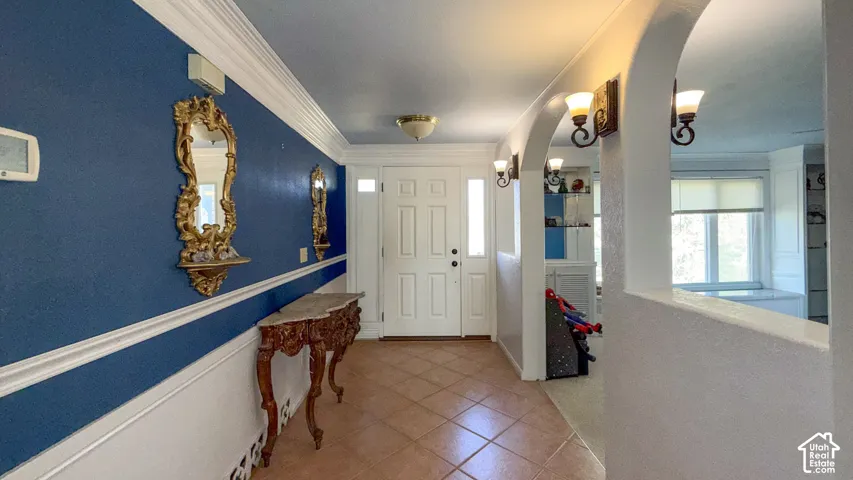 Entrance foyer featuring arched walkways, light tile patterned floors, and ornamental molding