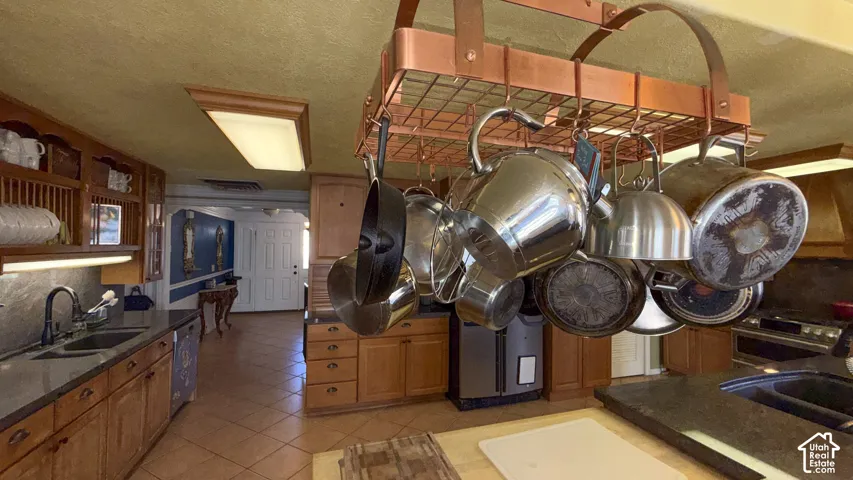 Kitchen featuring wood finish cabinetry, light tile patterned flooring, dishwasher, dark stone countertops, and backsplash