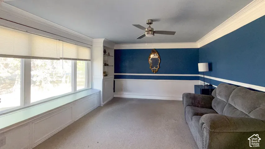 Living area with wainscoting, ornamental molding, ceiling fan, and carpet flooring