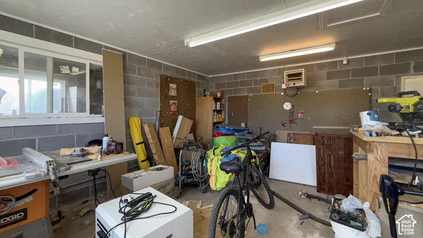 Garage with concrete block wall, a heating unit, a workshop area, and white refrigerator
