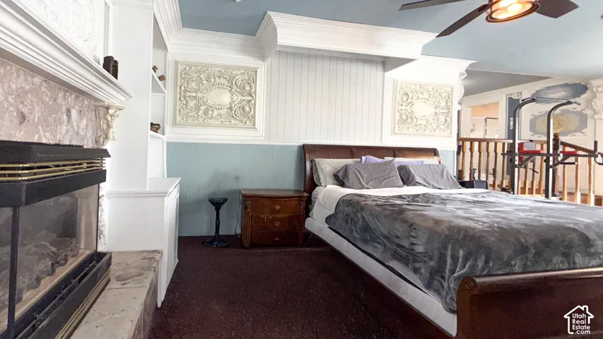 Bedroom with a fireplace with raised hearth, carpet floors, ornamental molding, ceiling fan, and wooden walls
