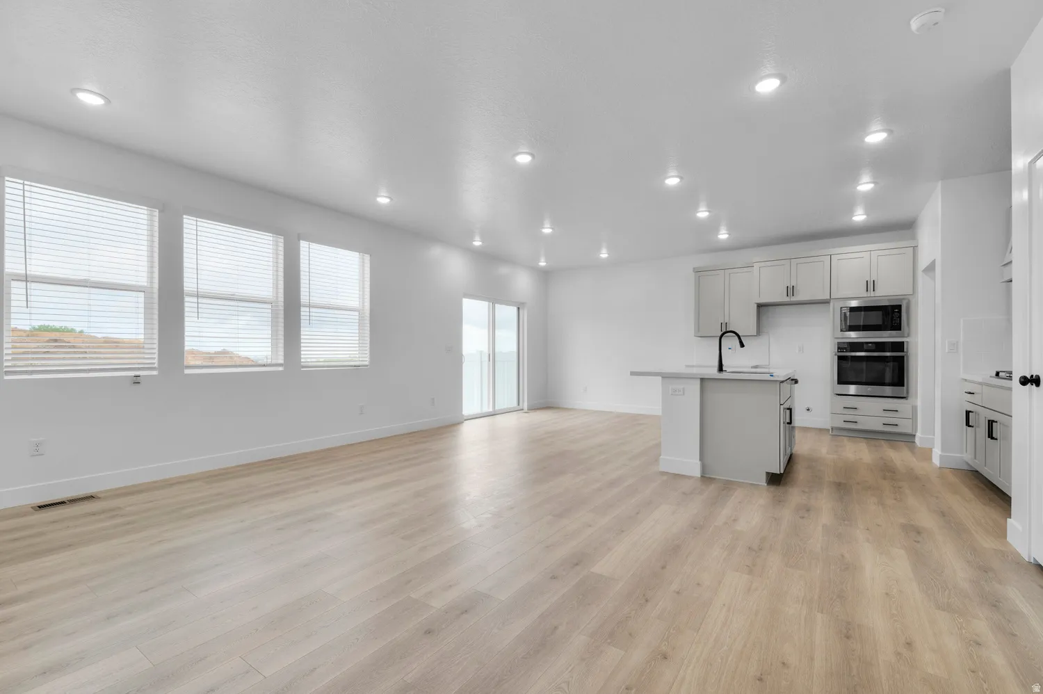 Kitchen featuring an island with sink, open floor plan, stainless steel appliances, light wood-style flooring, and recessed lighting