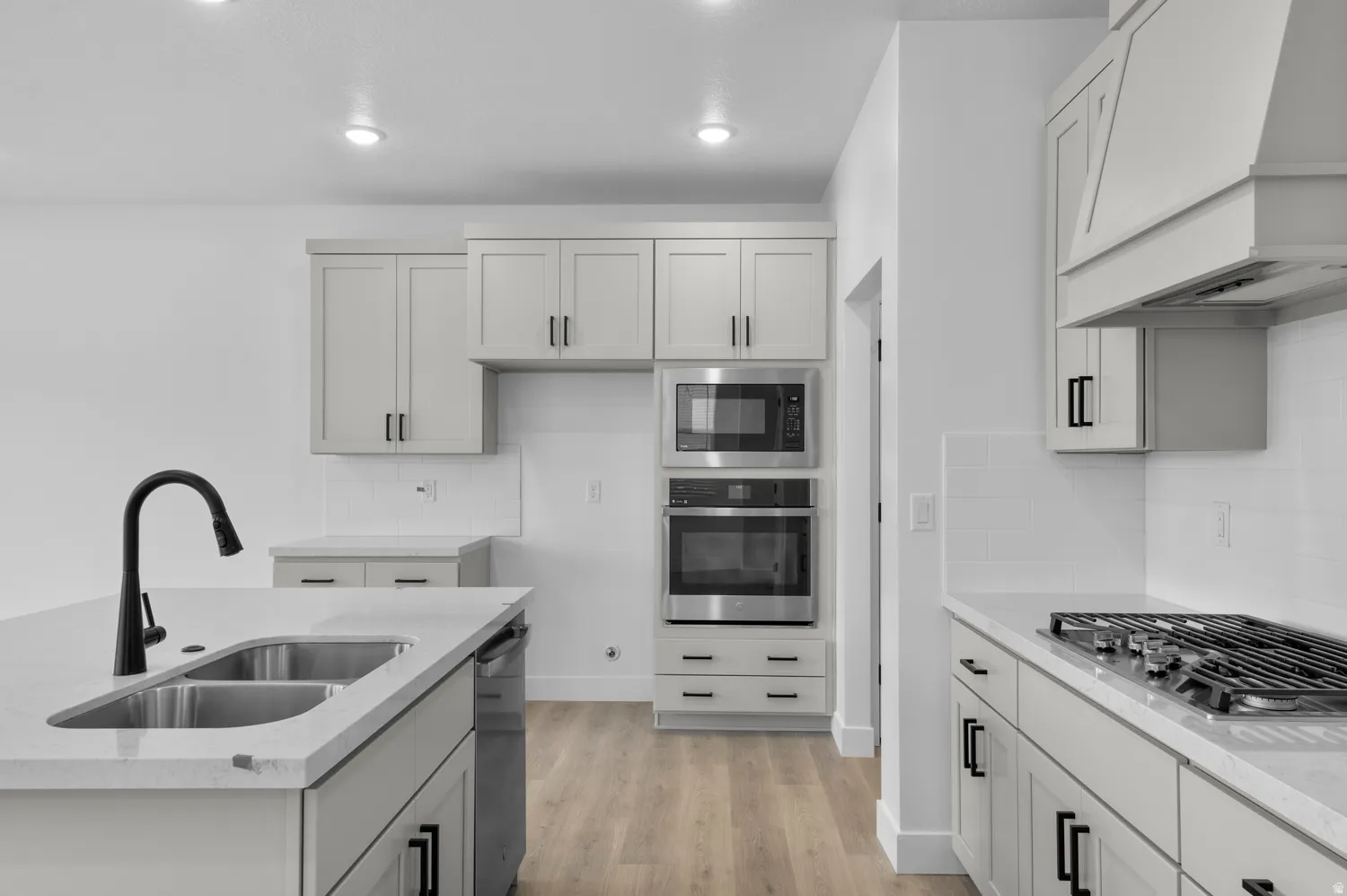 Kitchen featuring stainless steel appliances, light wood finished floors, light stone countertops, backsplash, and a center island with sink