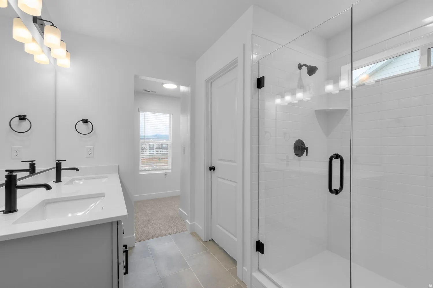 Bathroom featuring double vanity, a stall shower, light tile patterned floors, and light colored carpet