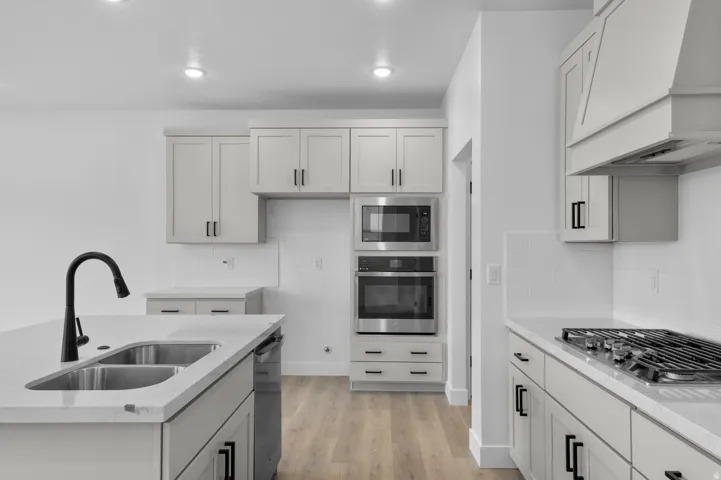 Kitchen featuring stainless steel appliances, light wood finished floors, light stone countertops, backsplash, and a center island with sink