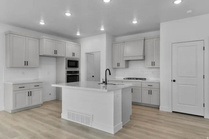Kitchen with a center island with sink, light stone countertops, light wood finished floors, stainless steel appliances, and recessed lighting