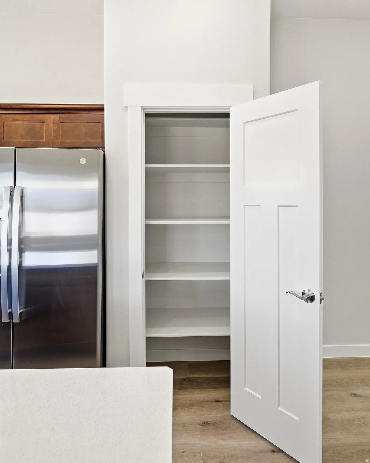 Built-in pantry with white shelving, stainless steel refrigerator, wood-finish flooring, and white countertops