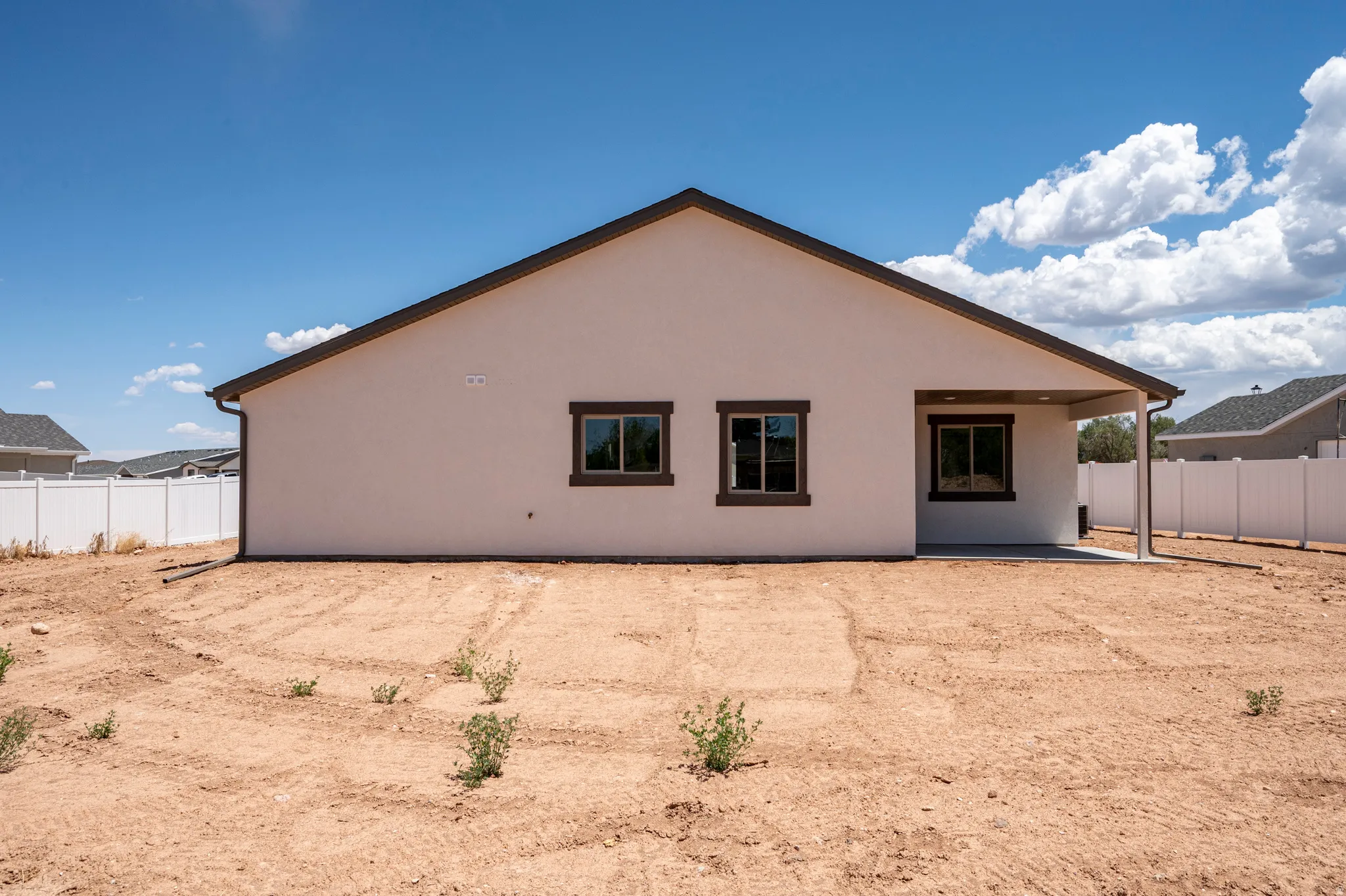 Expansive rear yard with a covered patio, white privacy fencing, stucco exterior, and dark-trimmed windows