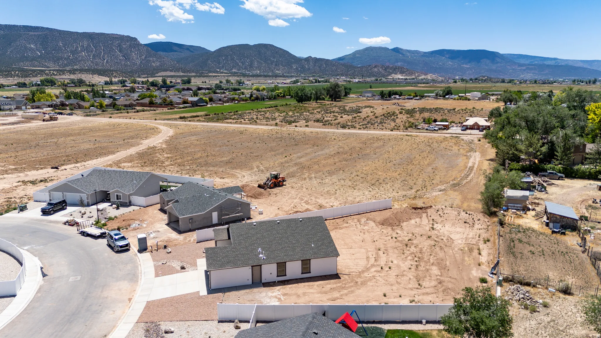 Expansive land parcel featuring existing residential structures, paved streets, and mountainous surroundings