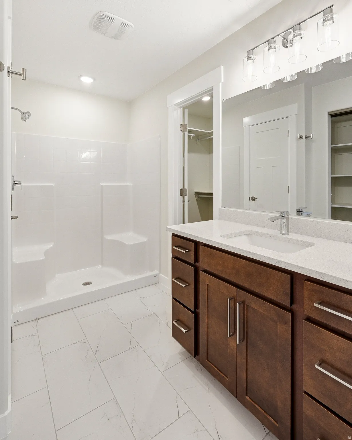 Double vanity with integrated sink and chrome fixtures, white countertop, dark wood-finish cabinetry, and large mirror with modern light fixture