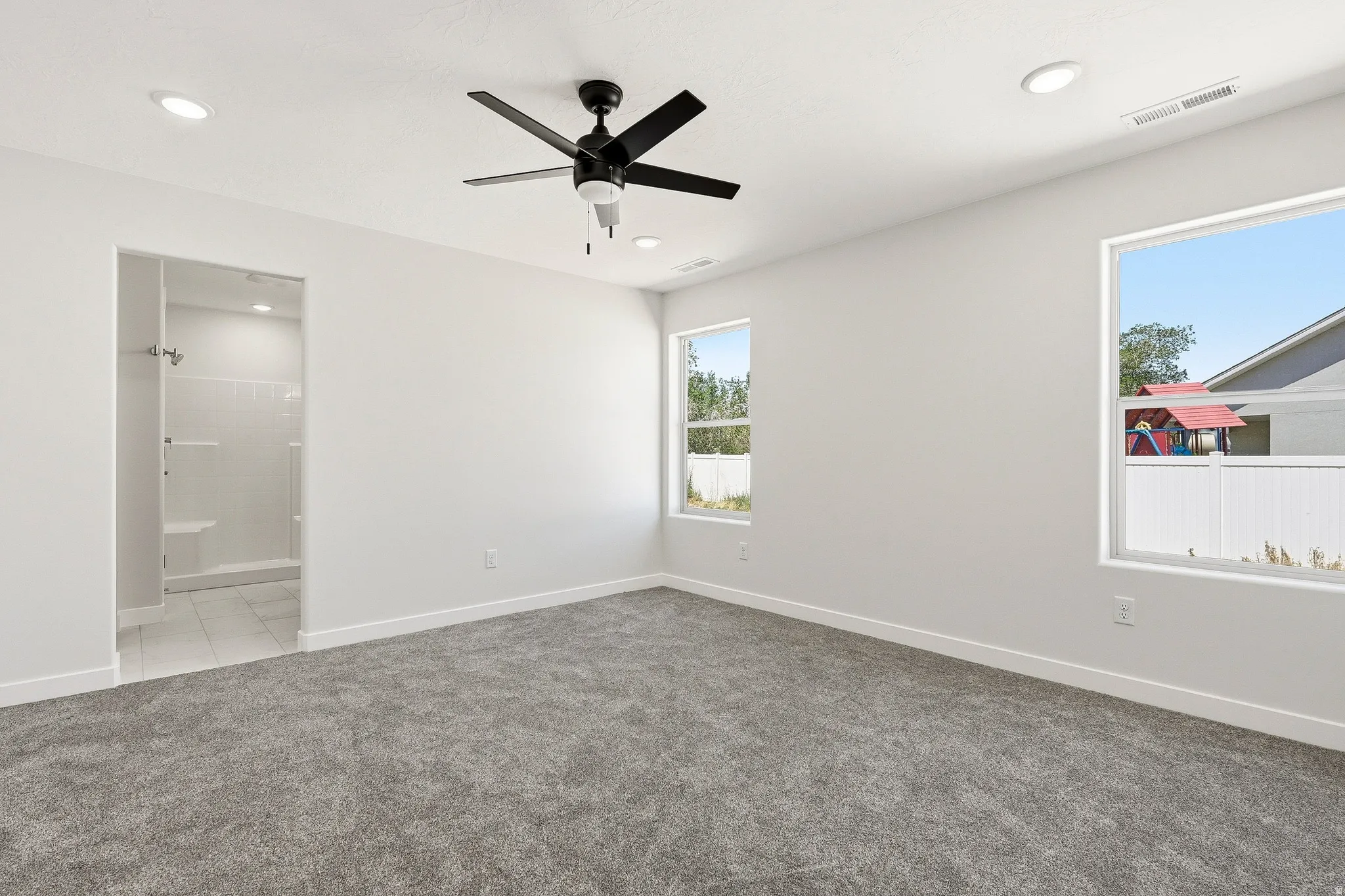 Recessed lighting, ceiling fan, two windows, wall-to-wall carpeting, and an adjacent tiled shower with a built-in bench