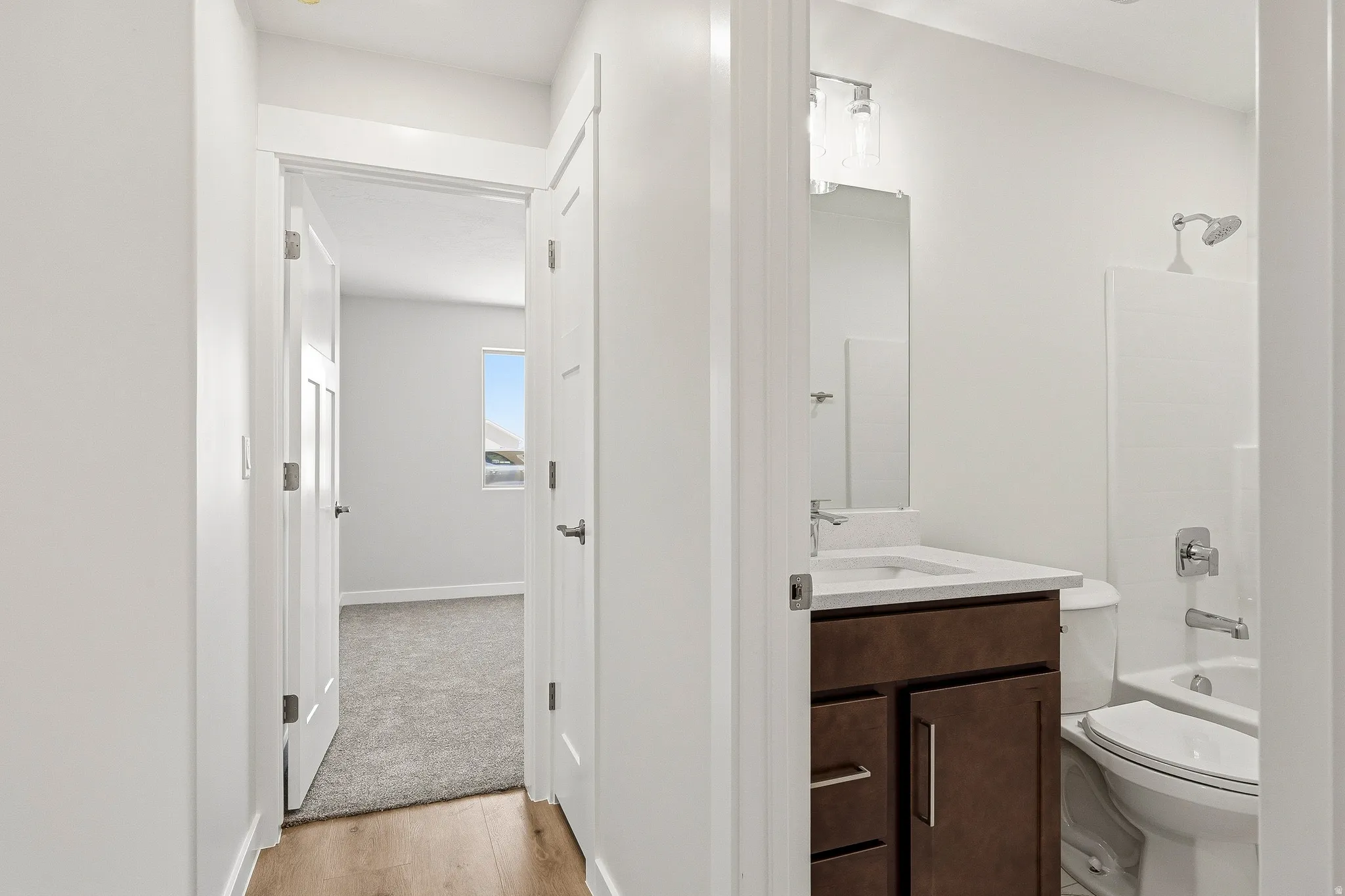 Wood-finish flooring, white walls, white doors, dark wood vanity, and a white sink