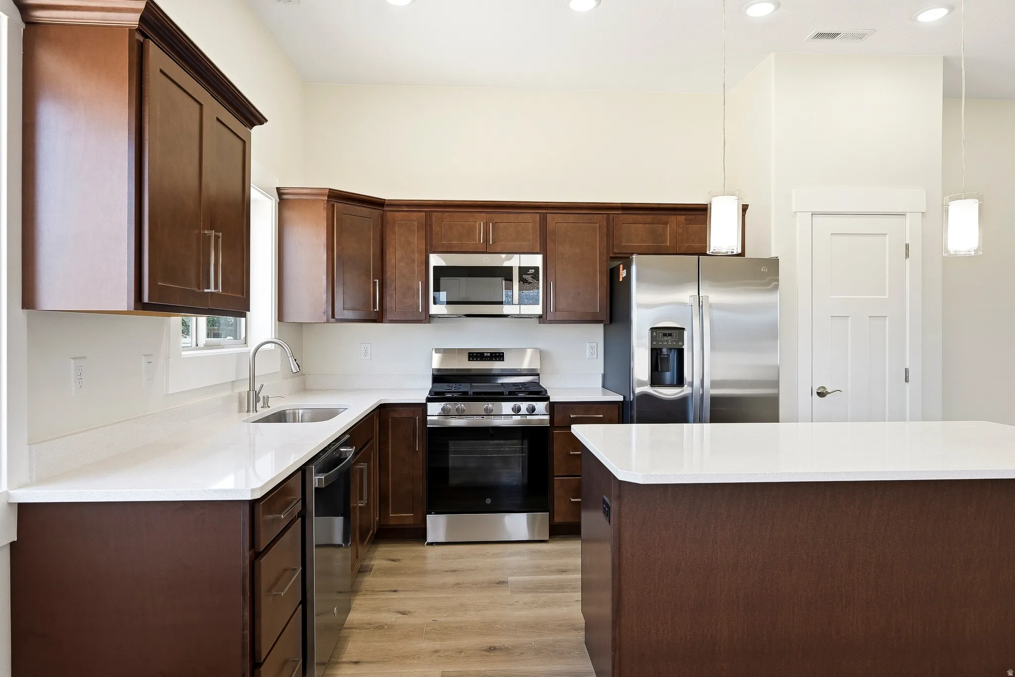 Kitchen featuring wood-finish cabinetry, stainless steel appliances, white countertops, and wood-finish flooring