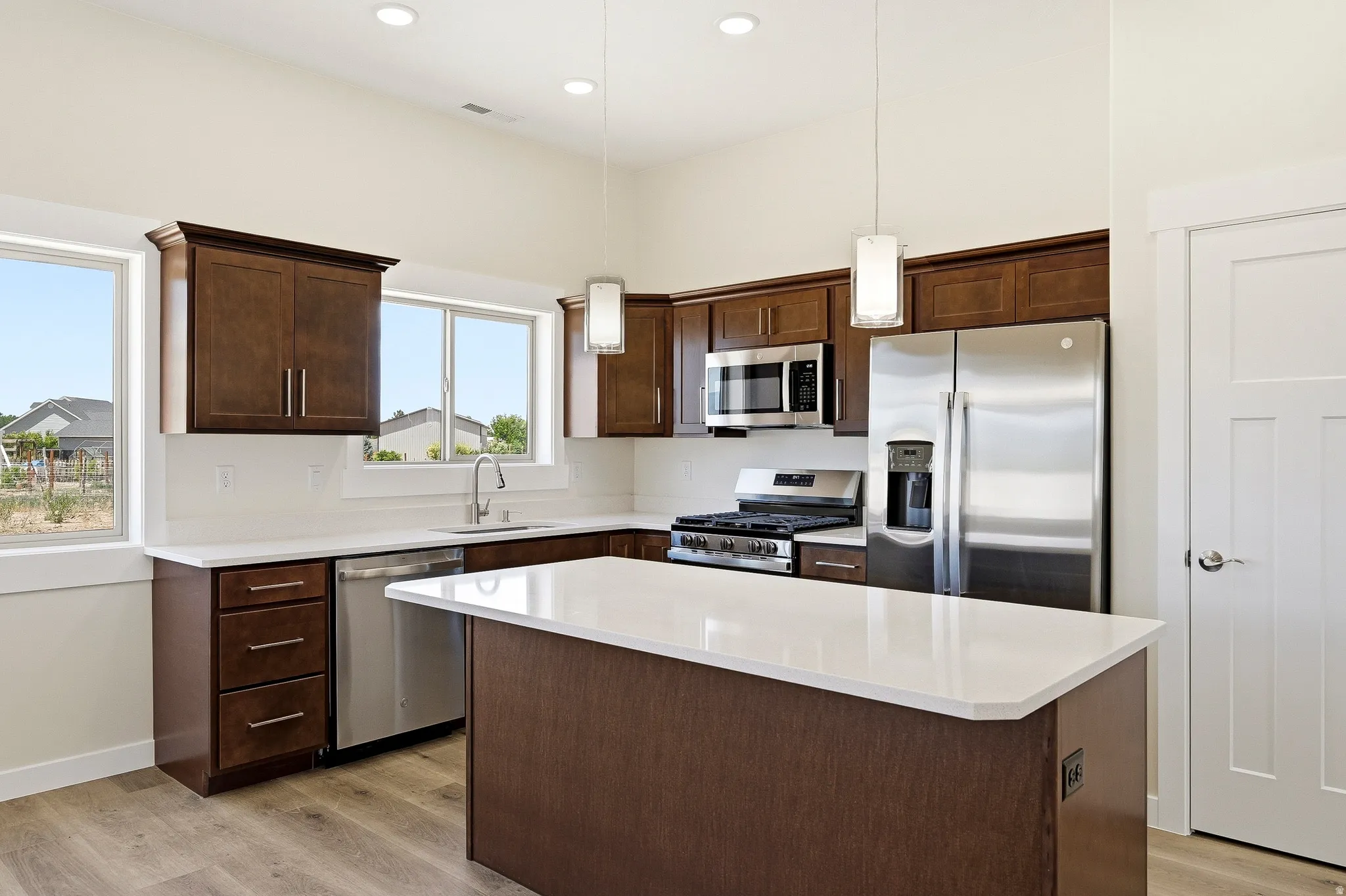 Kitchen with wood-finish flooring, dark wood cabinetry, stainless steel appliances, white countertops, and a central island