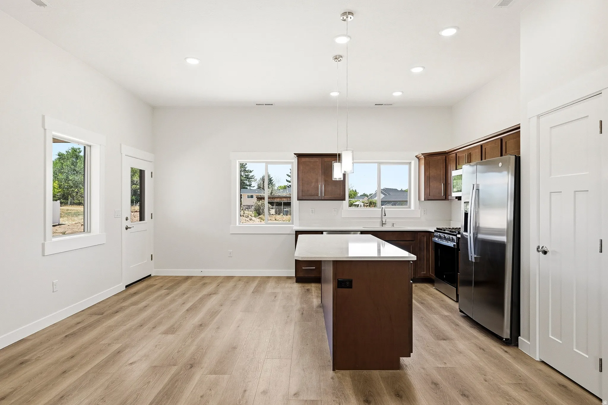 Open-concept kitchen with wood-finish flooring, stainless steel appliances, a center island, recessed lighting, and ample cabinetry