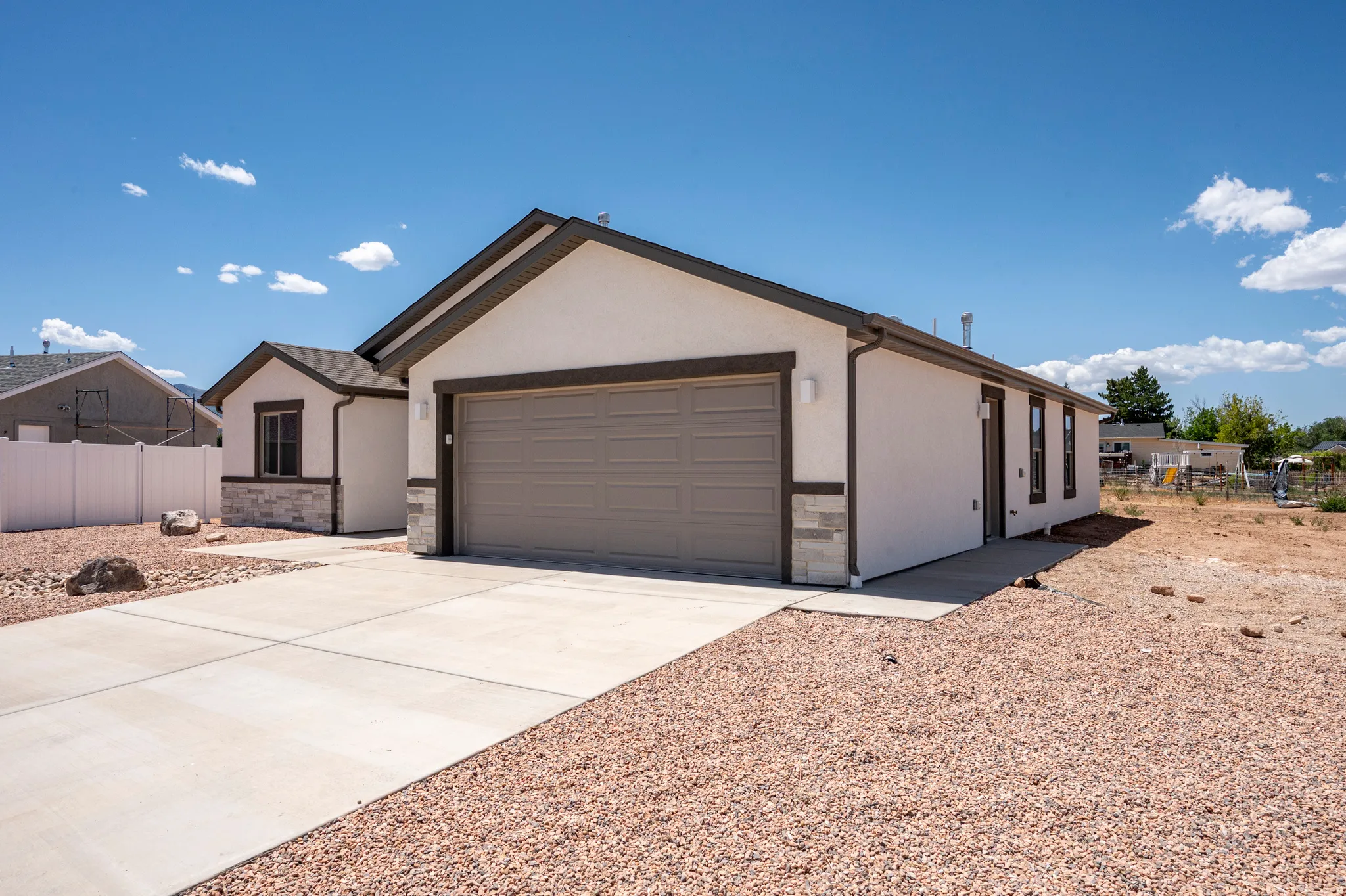 Modern stucco exterior with contrasting trim accents, stone veneer detailing, an attached two-car garage with a panel door, and a concrete driveway