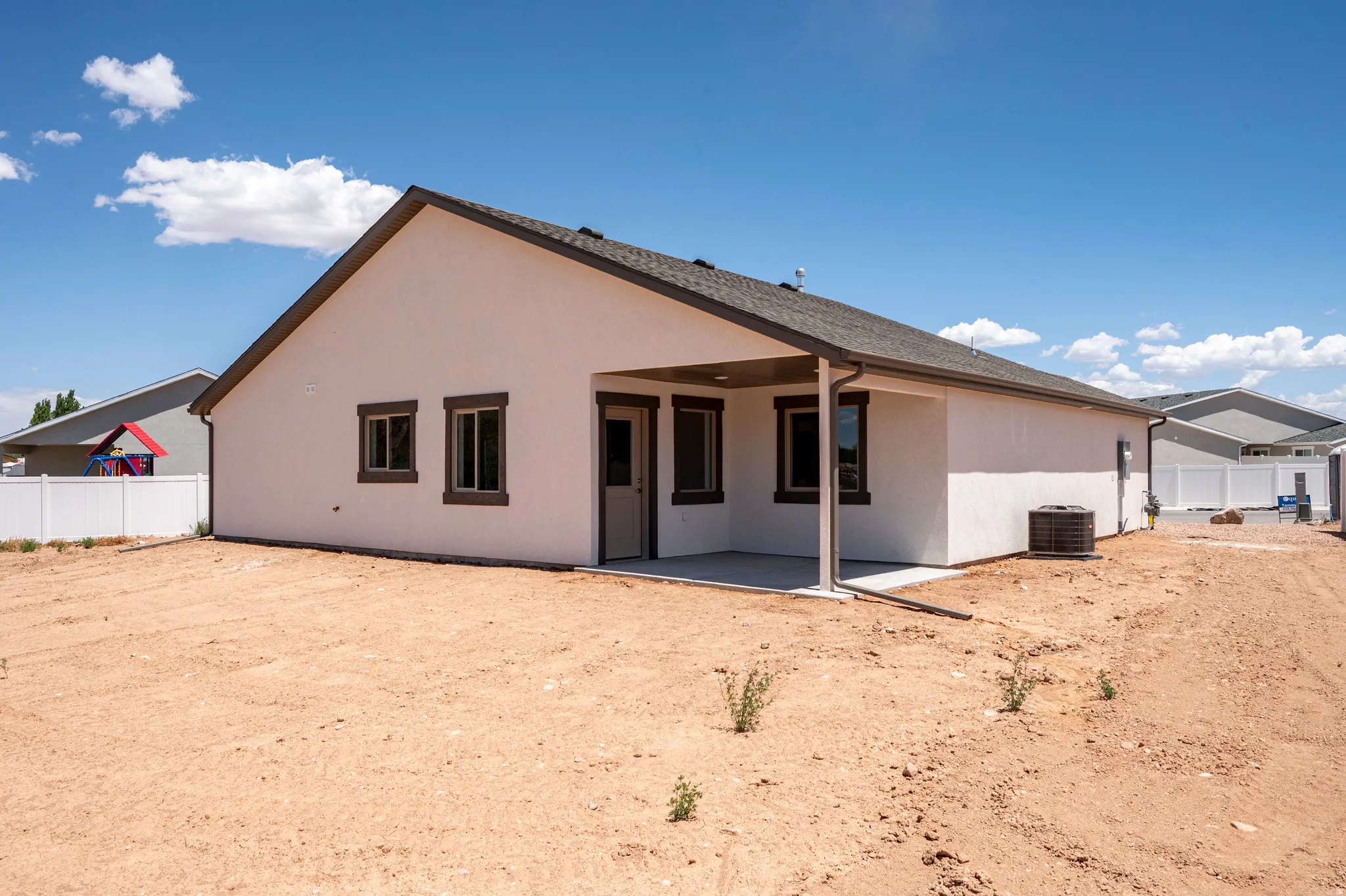Stucco exterior with a covered patio, dark framed windows, and a white vinyl fence