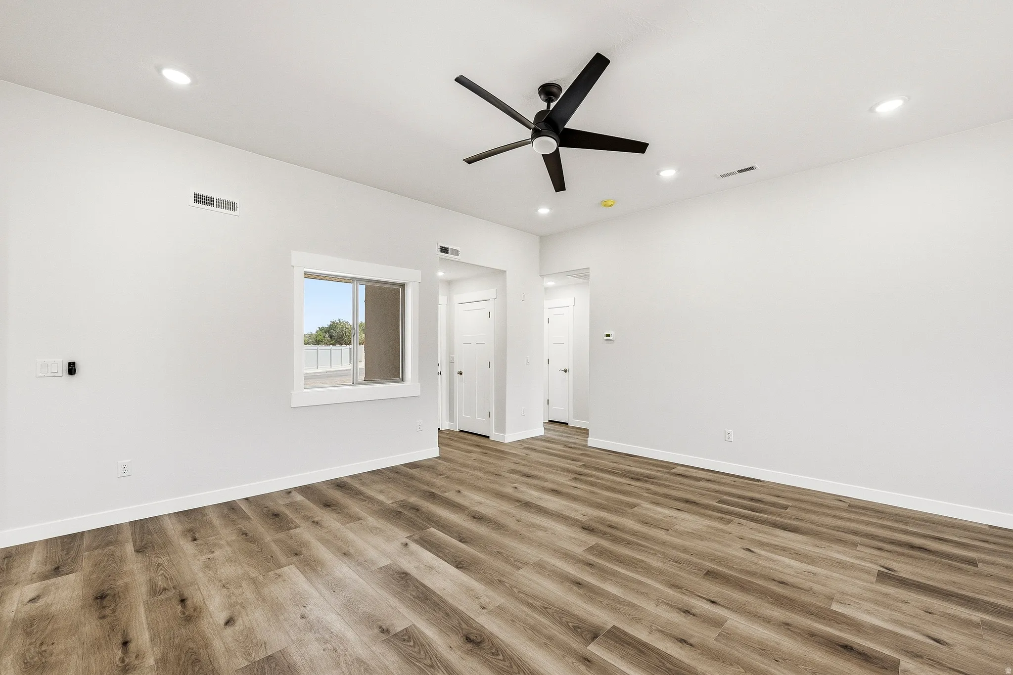 Spacious room featuring wood-finish flooring, a contemporary ceiling fan, recessed lighting, and a white-trimmed window