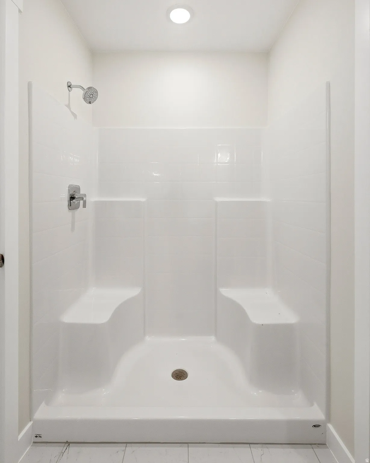 White shower enclosure with built-in seating, chrome fixtures, and a recessed ceiling light