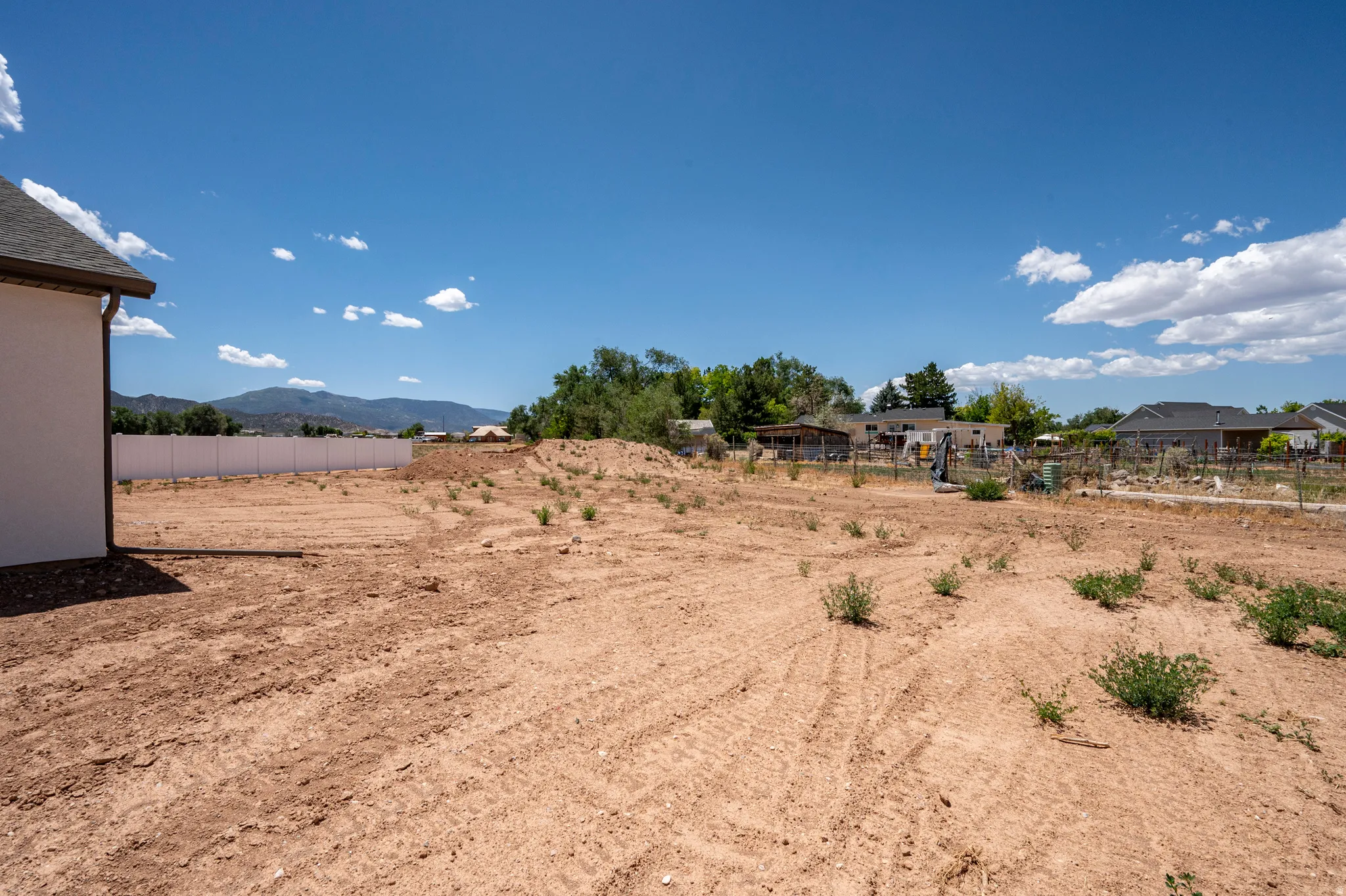 Expansive open lot with a mountain backdrop, featuring a white privacy fence and a partial building structure