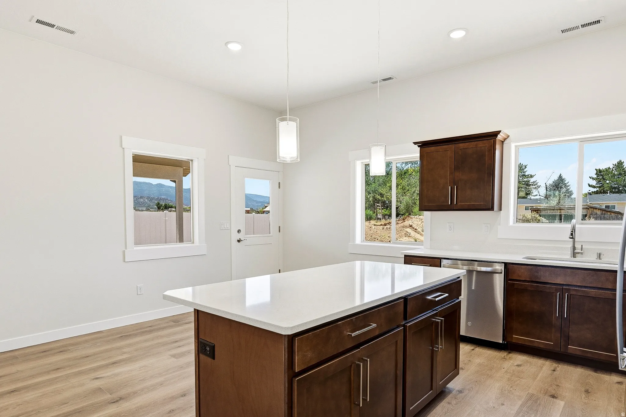 Kitchen featuring a central island with a light-toned countertop, wood-finish flooring, dark wood cabinetry, and stainless steel appliances