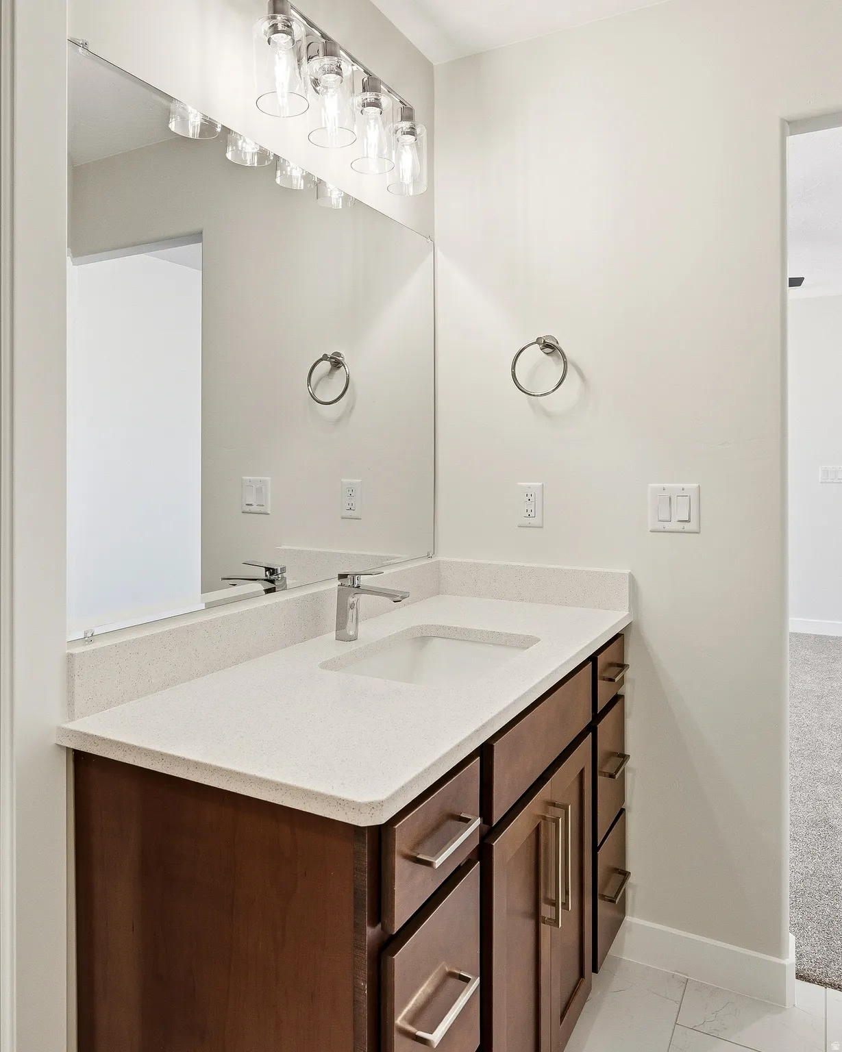 Built-in vanity with wood-finish cabinetry, light-toned countertop, integrated sink, and modern faucet