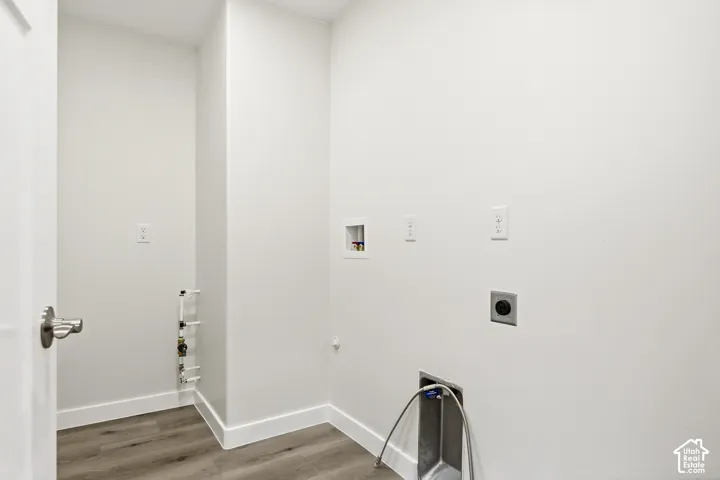 Wood-finish flooring with white baseboards, utility sink with flexible hose, appliance hookups, and a white interior door with brushed nickel hardware