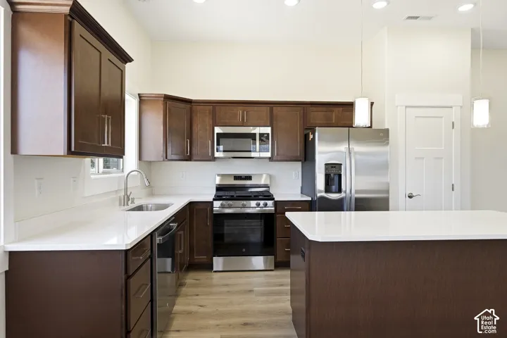 Kitchen featuring wood-finish cabinetry, stainless steel appliances, white countertops, and wood-finish flooring