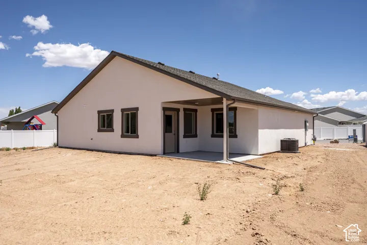 Stucco exterior with a covered patio, dark framed windows, and a white vinyl fence