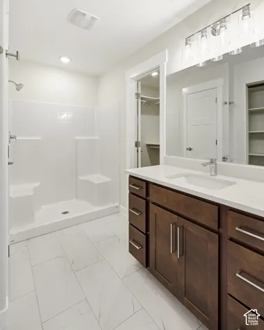 Double vanity with integrated sink and chrome fixtures, white countertop, dark wood-finish cabinetry, and large mirror with modern light fixture