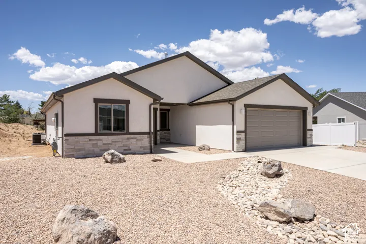 Stucco exterior with stone accent detailing, covered entrance, attached garage, and concrete driveway