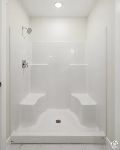 White shower enclosure with built-in seating, chrome fixtures, and a recessed ceiling light