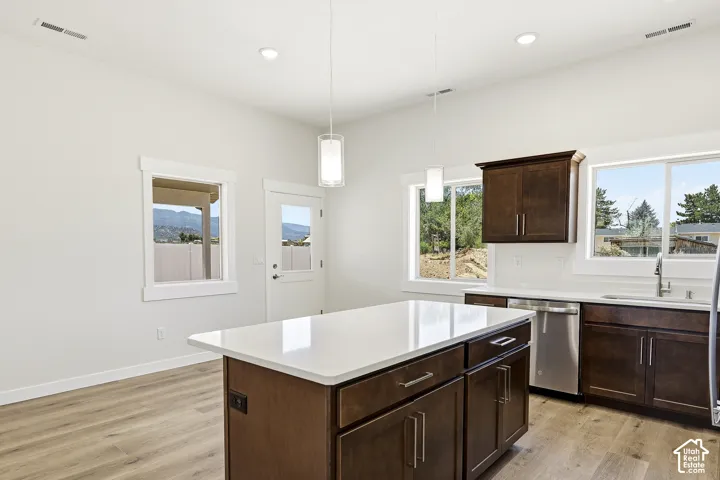 Kitchen featuring a central island with a light-toned countertop, wood-finish flooring, dark wood cabinetry, and stainless steel appliances