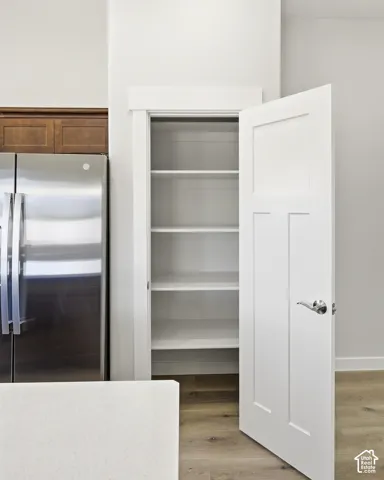 Built-in pantry with white shelving, stainless steel refrigerator, wood-finish flooring, and white countertops