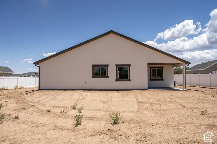 Expansive rear yard with a covered patio, white privacy fencing, stucco exterior, and dark-trimmed windows