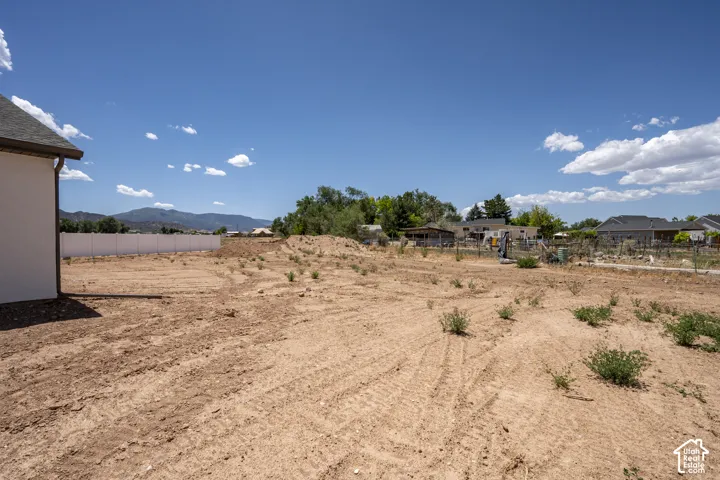 Expansive open lot with a mountain backdrop, featuring a white privacy fence and a partial building structure