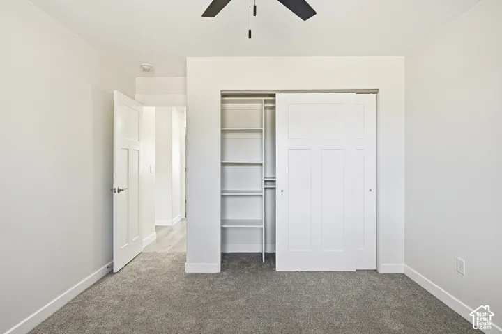 Plush carpet flooring, white painted walls, ceiling fan, sliding closet door with built-in shelving, and a paneled interior door