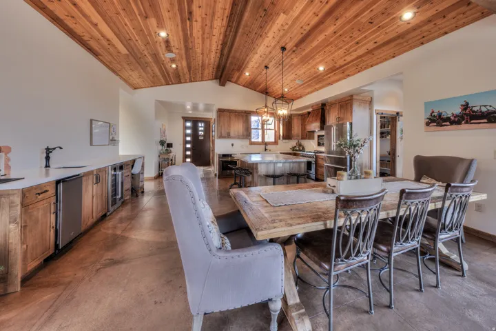 Dining area with finished concrete floors, beverage cooler, hanging lights, and a high wooden beamed ceiling