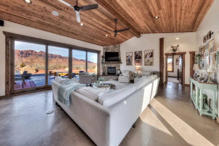 Living room with a ceiling fan, concrete flooring, a high wood beamed ceiling, recessed lighting, and a stone fireplace