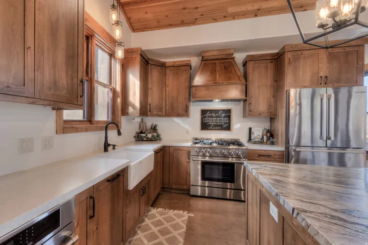 Kitchen featuring stainless steel appliances, wood finish cabinetry, pendant lighting, wood ceiling, and light stone counters