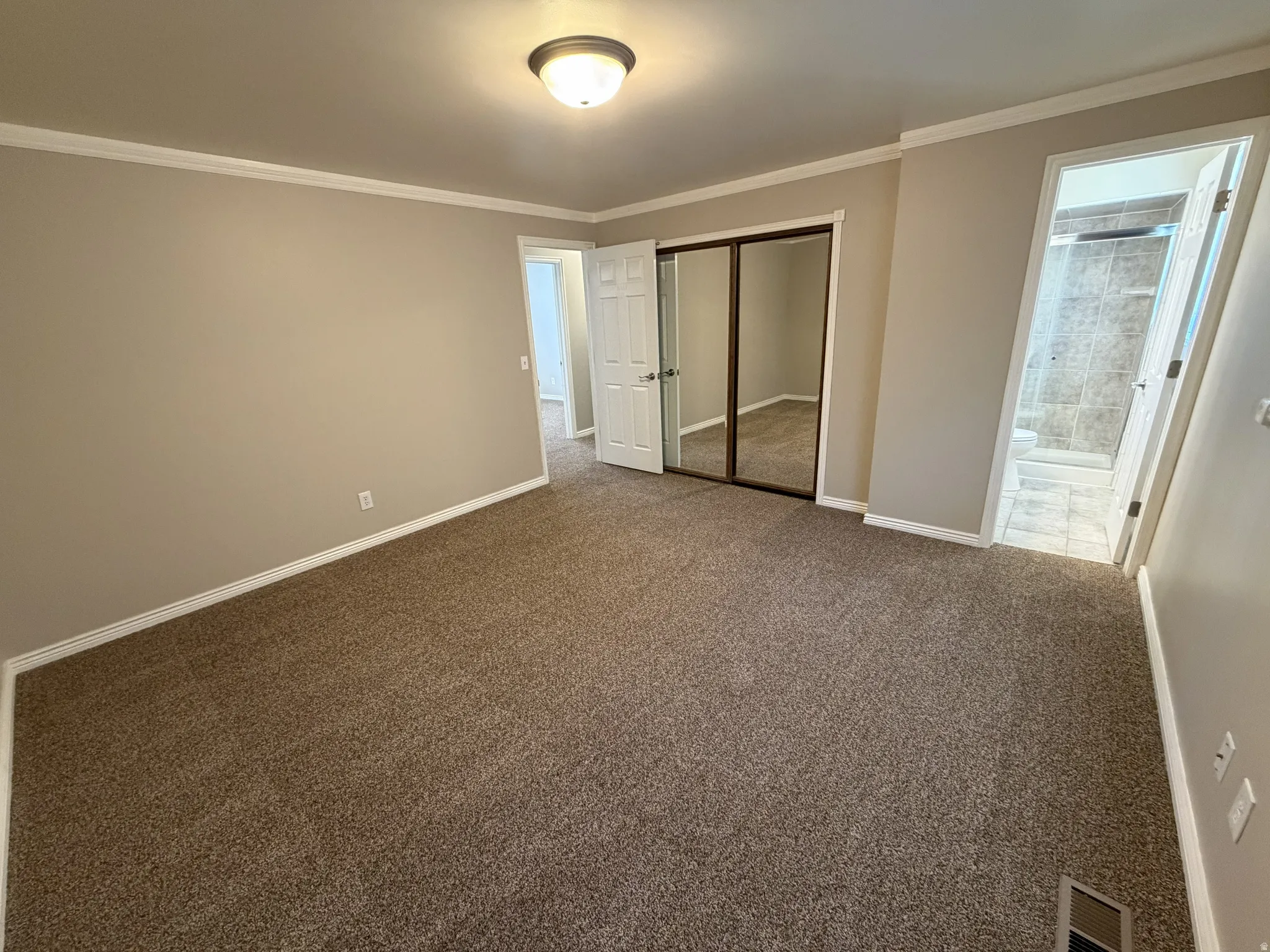 Main suite bedroom featuring crown molding, dark colored carpet, closet with mirror doors and entrance to main suite bath